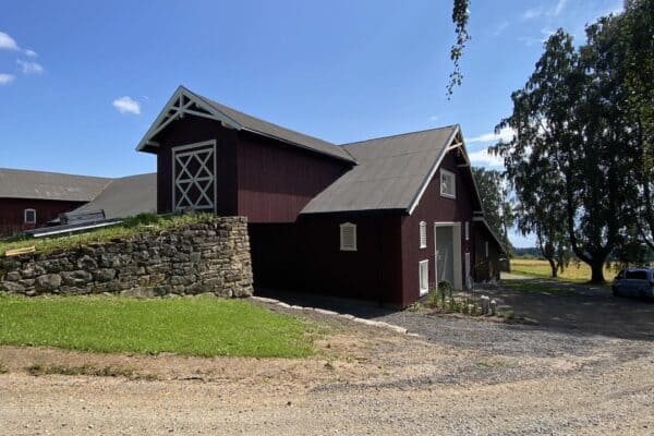Landsbruksbygg i treverk med tradisjonell design og rødmalte vegger, omgitt av grøntarealer og åpen himmel, perfekt for landbruksformål og eiendomsutvikling i Innlandet.